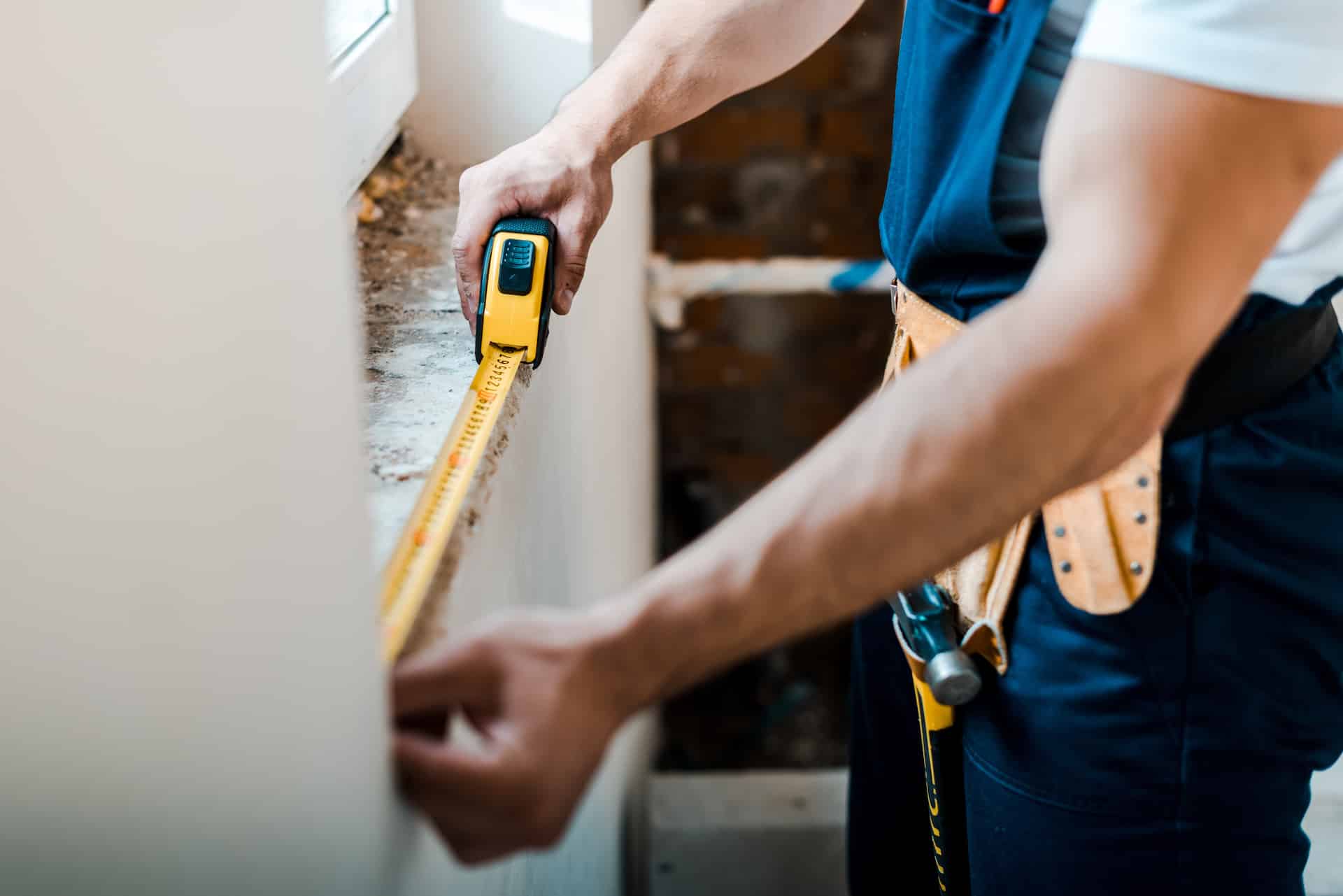 cropped view of handyman measuring wall with yellow measuring tape Cottage Builders Winnipeg MB